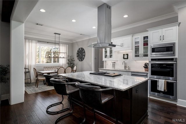 kitchen featuring white cabinets, a breakfast bar area, island range hood, a kitchen island, and appliances with stainless steel finishes