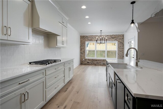 13947 Glenview Dr, Northport, AL 35475 - kitchen with stainless steel gas cooktop, custom range hood, a sink, brick wall, and light wood-style flooring
