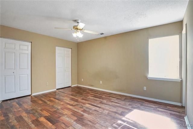 unfurnished bedroom featuring hardwood / wood-style floors, a textured ceiling, multiple closets, and ceiling fan