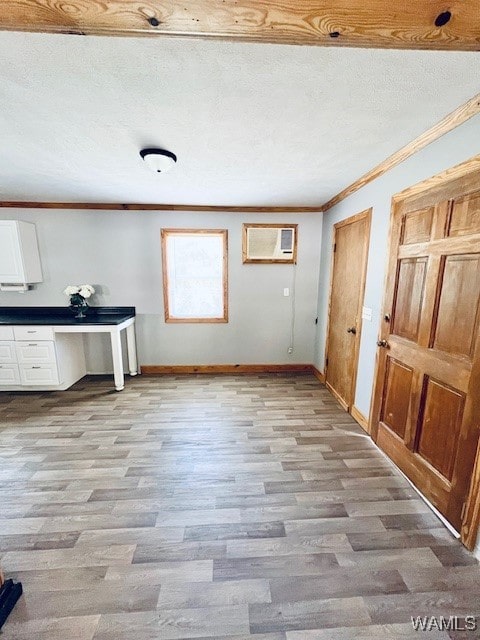 interior space with a wall mounted air conditioner, light hardwood / wood-style floors, a textured ceiling, white cabinets, and ornamental molding