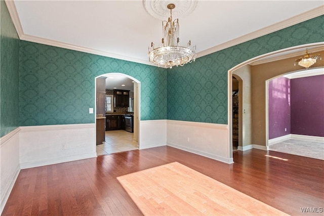 empty room with crown molding, hardwood / wood-style floors, and a notable chandelier