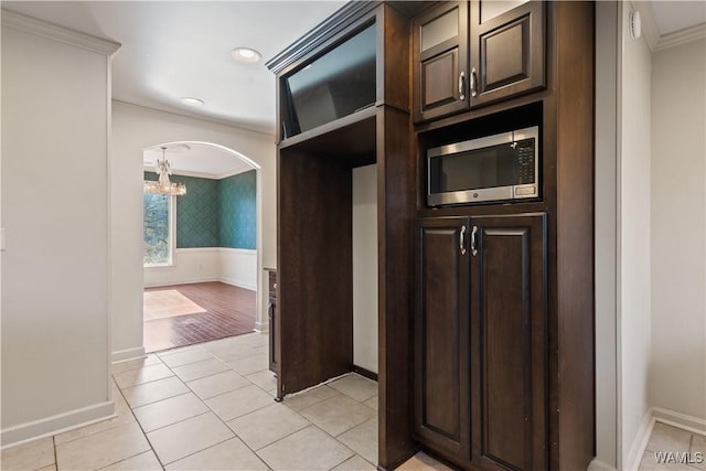 kitchen featuring dark brown cabinetry, ornamental molding, a notable chandelier, and light tile patterned floors