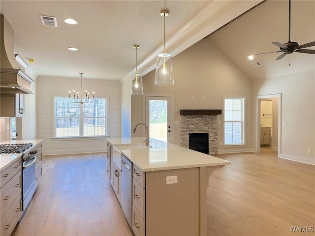 kitchen with an island with sink, stainless steel appliances, a fireplace, hanging light fixtures, and ceiling fan with notable chandelier