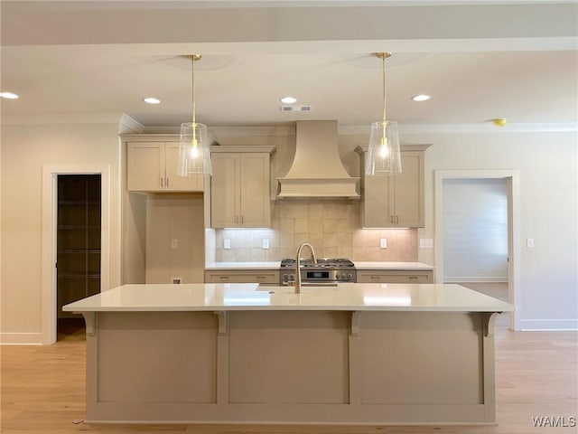 kitchen with light wood-type flooring, a kitchen island with sink, pendant lighting, and custom range hood