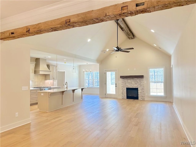 unfurnished living room with a fireplace, light hardwood / wood-style floors, beamed ceiling, high vaulted ceiling, and ceiling fan with notable chandelier