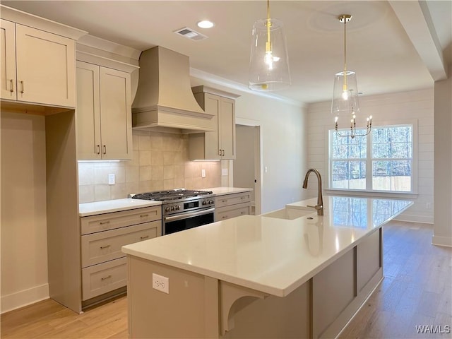 kitchen featuring pendant lighting, premium range hood, sink, a kitchen island with sink, and stainless steel range with gas cooktop