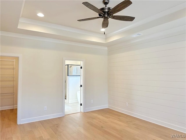 unfurnished room with ceiling fan, a tray ceiling, and light wood-type flooring