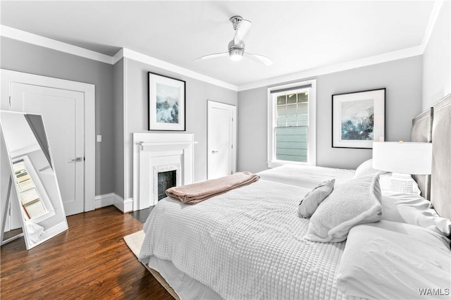 bedroom with dark wood-type flooring, a fireplace, a ceiling fan, baseboards, and crown molding