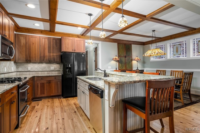 kitchen with appliances with stainless steel finishes, a kitchen island with sink, coffered ceiling, and sink