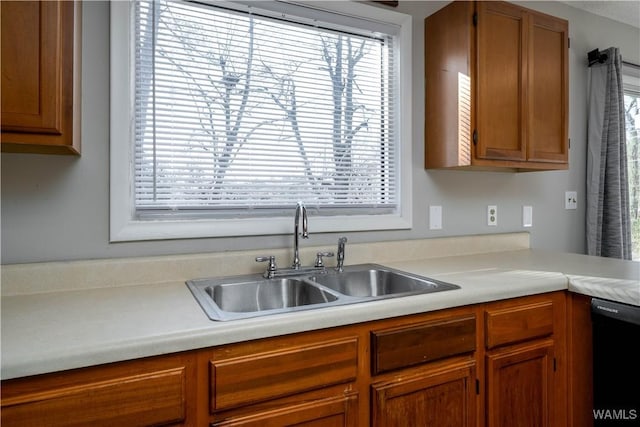 kitchen featuring black dishwasher, light countertops, brown cabinetry, and a sink