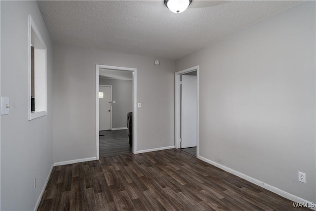 unfurnished room with a textured ceiling, dark wood finished floors, and baseboards