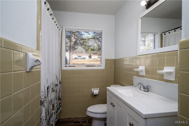 bathroom featuring a textured ceiling, toilet, visible vents, tile walls, and wainscoting