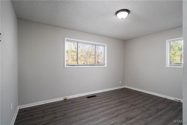 empty room featuring a textured ceiling, dark wood-style flooring, visible vents, and baseboards