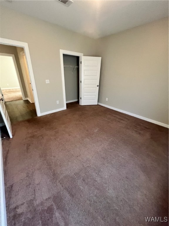 unfurnished bedroom with dark colored carpet and a closet