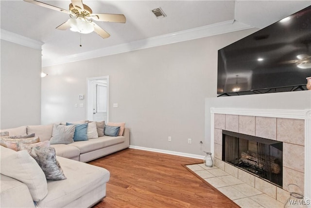 living room featuring visible vents, a ceiling fan, a tiled fireplace, ornamental molding, and wood finished floors