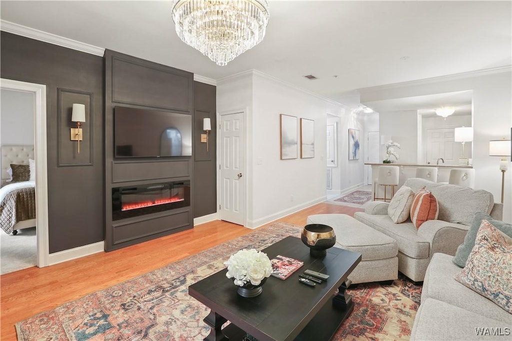 living room featuring hardwood / wood-style floors, crown molding, a large fireplace, and a chandelier