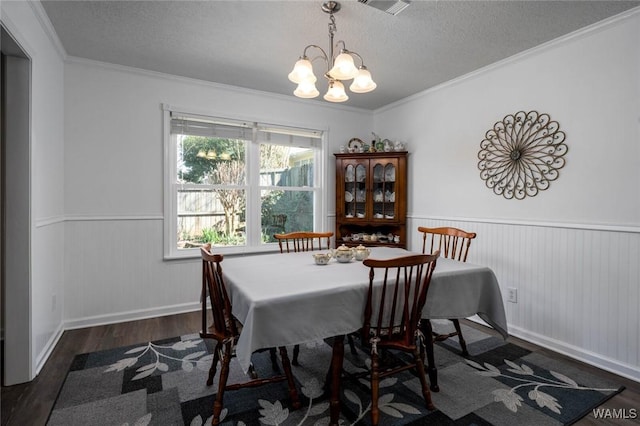 dining space featuring wainscoting, wood finished floors, crown molding, a textured ceiling, and a chandelier