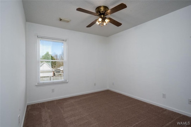 empty room with a textured ceiling, dark colored carpet, a ceiling fan, and baseboards