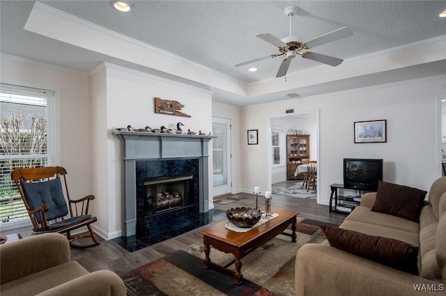 living area featuring a textured ceiling, a tray ceiling, dark wood finished floors, and crown molding