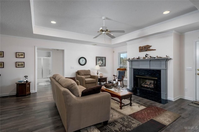 living room with a textured ceiling, a fireplace, dark wood-style floors, a tray ceiling, and crown molding