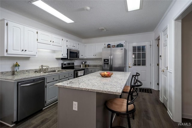 kitchen featuring a breakfast bar, a sink, appliances with stainless steel finishes, a center island, and dark wood-style floors