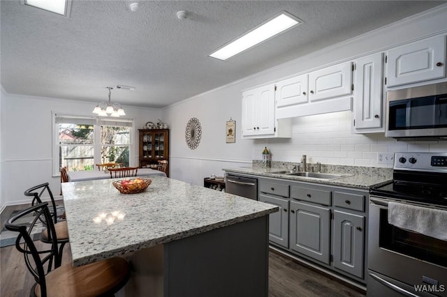 kitchen with a breakfast bar area, stainless steel appliances, a sink, gray cabinets, and dark wood finished floors