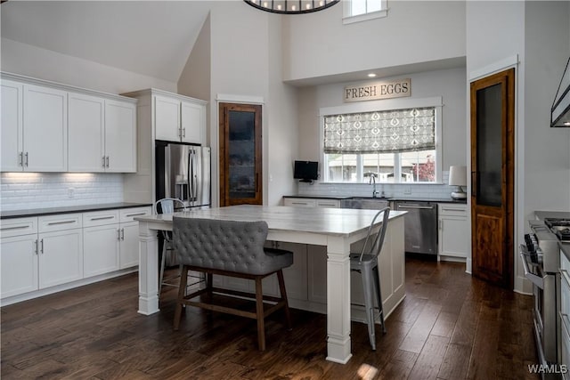 kitchen with tasteful backsplash, stainless steel appliances, a sink, white cabinetry, and high vaulted ceiling