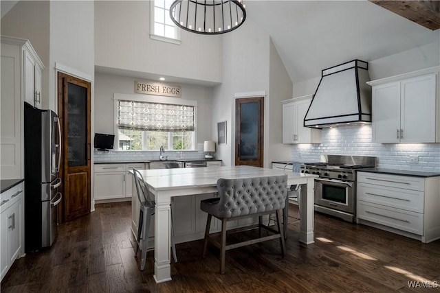 kitchen with dark wood-style flooring, stainless steel appliances, high vaulted ceiling, tasteful backsplash, and premium range hood