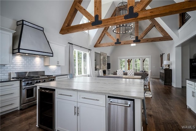 kitchen with custom range hood, high vaulted ceiling, high end stainless steel range oven, open floor plan, and beverage cooler