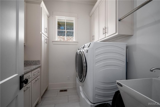 clothes washing area featuring a sink, cabinet space, light tile patterned floors, separate washer and dryer, and baseboards