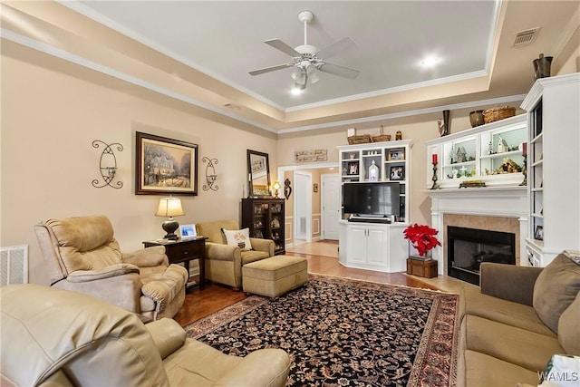 living room featuring a tray ceiling, ornamental molding, and a tile fireplace