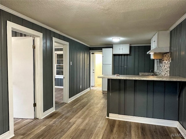 kitchen with kitchen peninsula, white cabinetry, wood-type flooring, and a textured ceiling