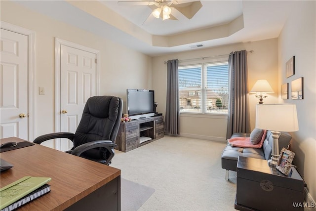 office area featuring a tray ceiling, visible vents, ceiling fan, and light carpet