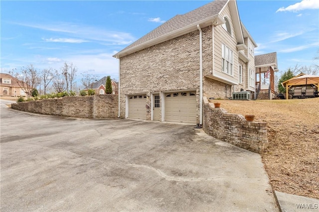 view of home's exterior featuring brick siding, driveway, an attached garage, and roof with shingles