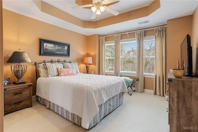 bedroom with ceiling fan, light colored carpet, visible vents, baseboards, and a tray ceiling