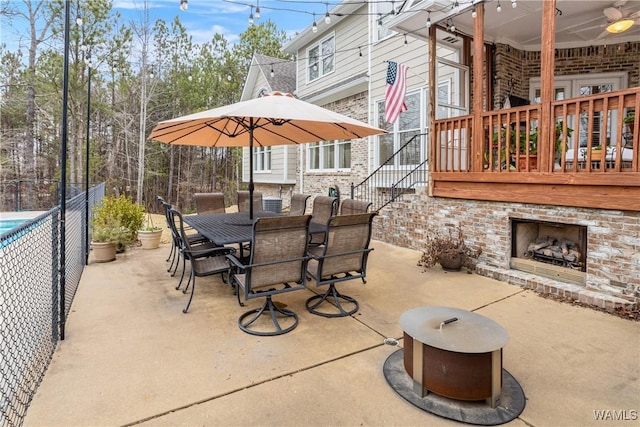 view of patio with an outdoor brick fireplace, stairway, outdoor dining space, and fence