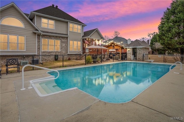 pool at dusk featuring a diving board, a patio area, fence, and a fenced in pool