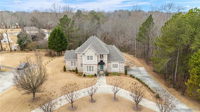 view of front of property featuring stone siding, driveway, and a wooded view