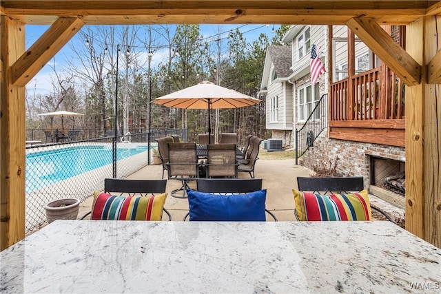 view of patio with a fenced in pool, outdoor dining area, central AC unit, fence, and an outdoor brick fireplace