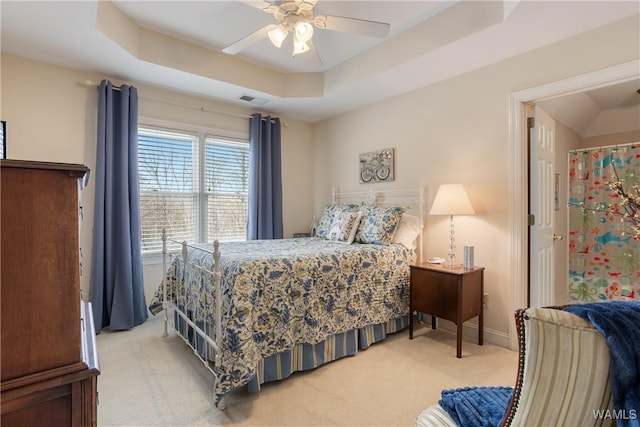 bedroom with light colored carpet, visible vents, baseboards, a ceiling fan, and a raised ceiling