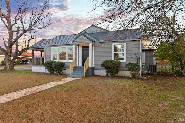 bungalow-style house with central air condition unit, metal roof, and a yard