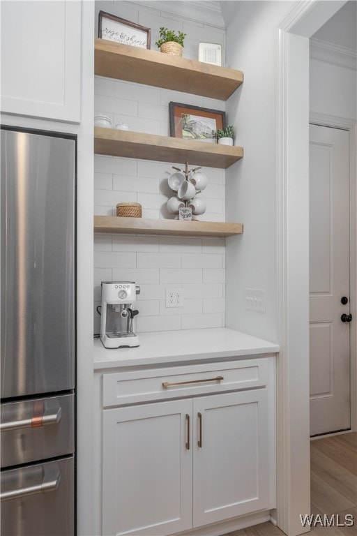 bar featuring white cabinetry, stainless steel fridge, and ornamental molding