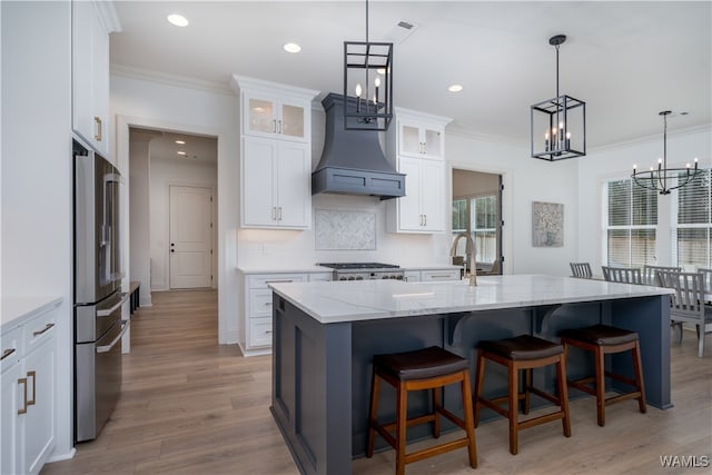 kitchen with appliances with stainless steel finishes, light wood-type flooring, pendant lighting, white cabinetry, and an island with sink