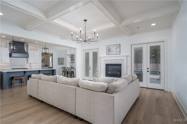 living room with french doors, light hardwood / wood-style floors, coffered ceiling, and beam ceiling