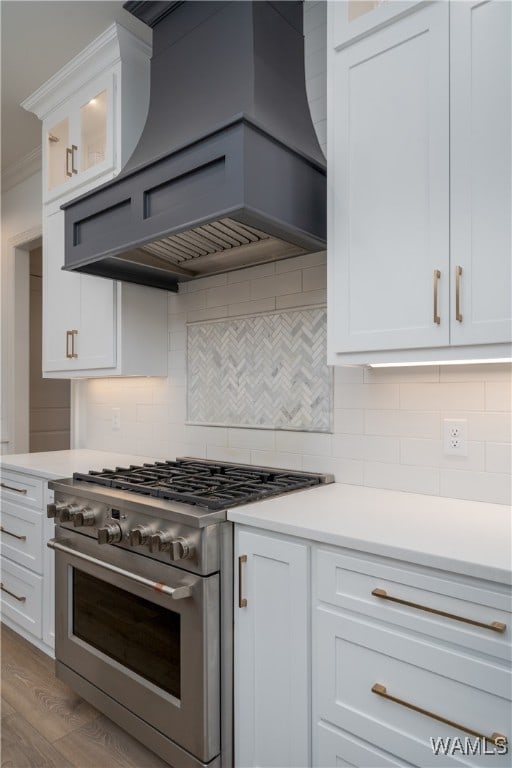 kitchen featuring decorative backsplash, premium range hood, high end stove, light hardwood / wood-style flooring, and white cabinets