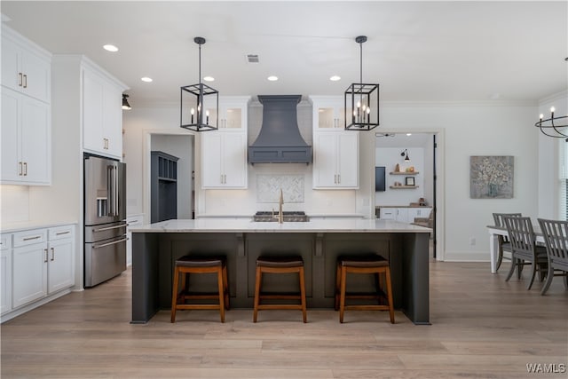 kitchen featuring stainless steel fridge with ice dispenser, white cabinetry, custom range hood, and an island with sink