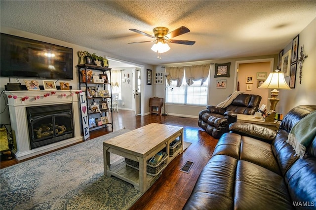 living room featuring ceiling fan, dark wood-type flooring, and a textured ceiling