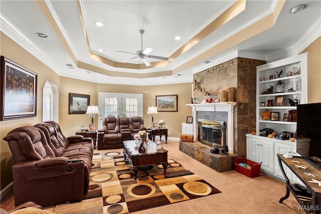 living area featuring arched walkways, a tray ceiling, a tiled fireplace, and crown molding