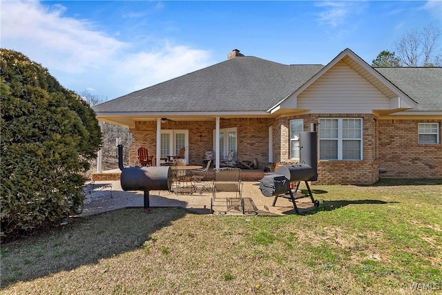 rear view of house featuring brick siding, a yard, a chimney, a patio, and a shingled roof