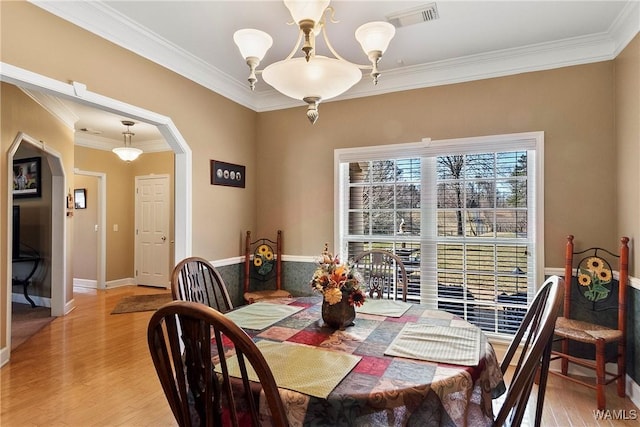 dining room with arched walkways, visible vents, light wood-style flooring, and an inviting chandelier